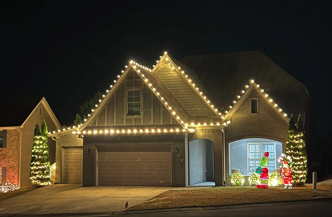 Gabled roof lines traced in warm bulbs with lit trees flanking the garage